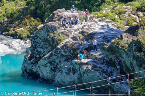 Visitors to Hokitika Gorge sitting on the rocks by the side of the river in the sun, West Coast, New Zealand