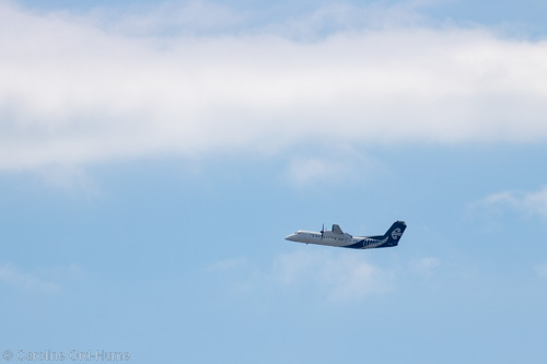 Air New Zealand plane flying through a blue sky with clouds above New Zealand
